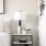 a nightstand with accessories next to a made bed